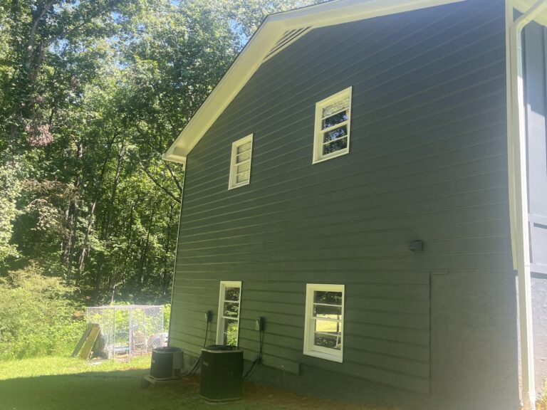 Two-story home exterior with green siding and white window trim completed by Roof Works