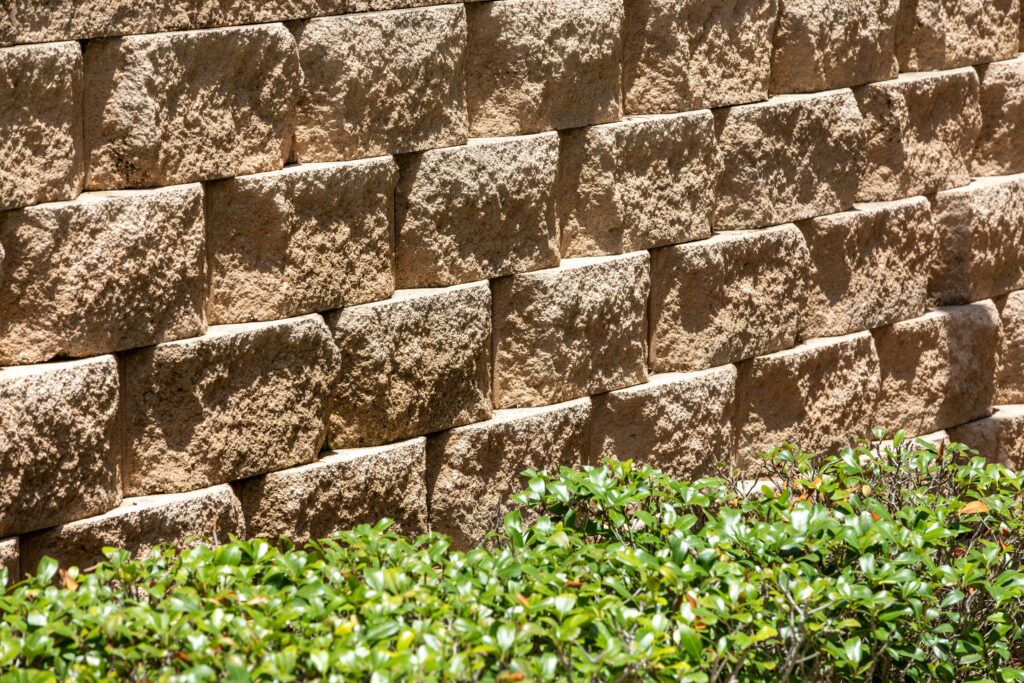 Close up of a tan segmental block retaining wall above a low green hedge