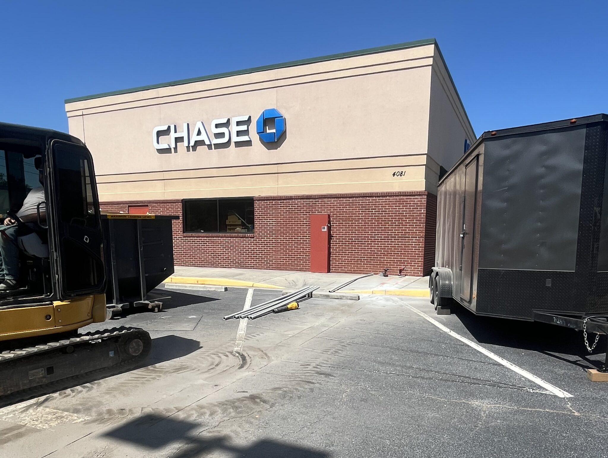 Excavator and enclosed work trailer staged for light commercial contracting at a storefront property