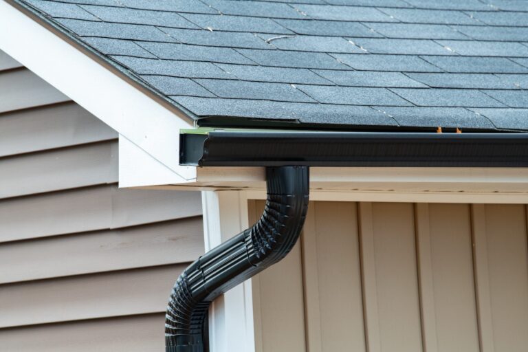 Black seamless gutter and downspout along a shingled roofline