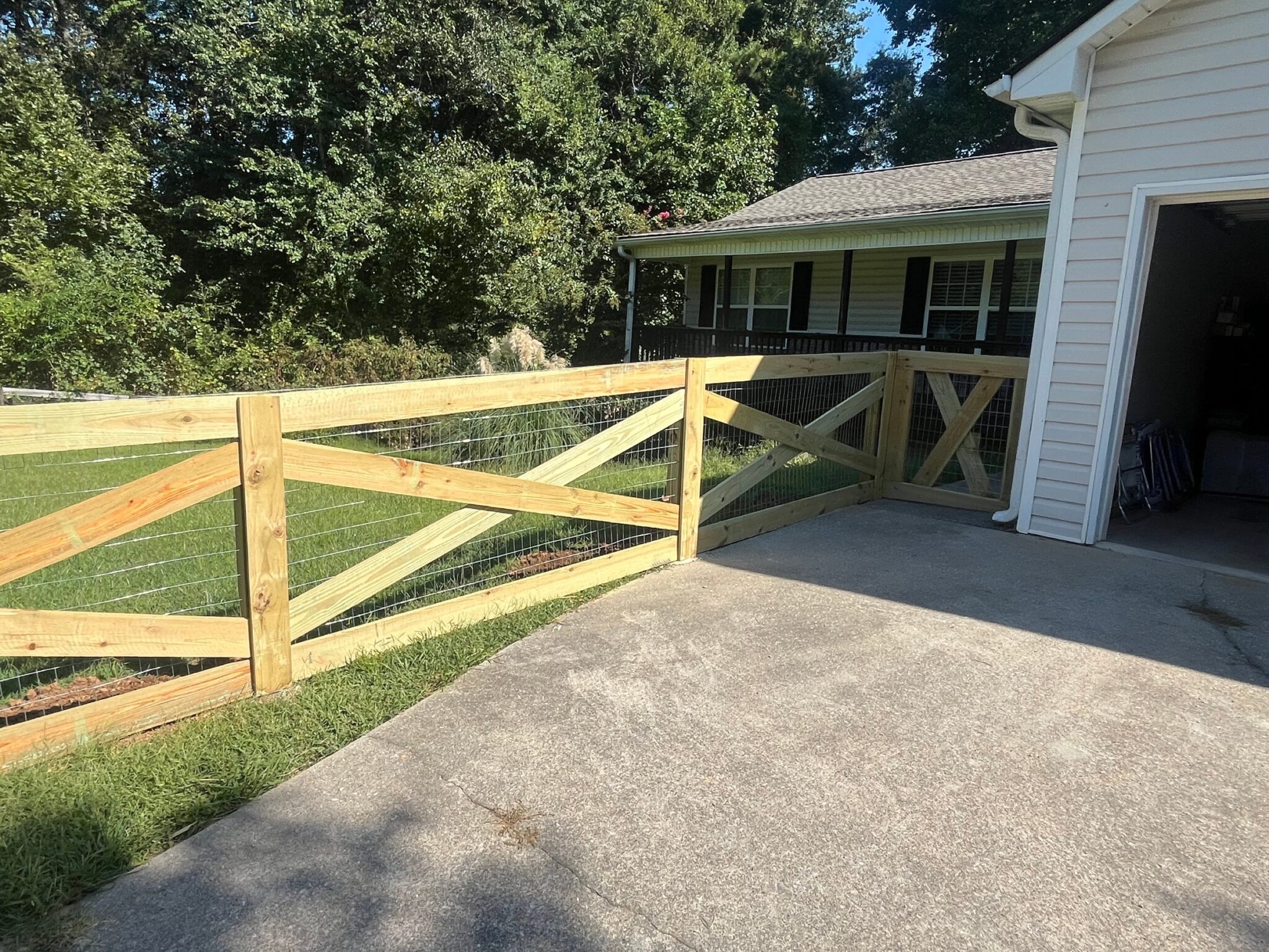Wood fence with cross buck panels and wire mesh meeting a drive gate beside a garage
