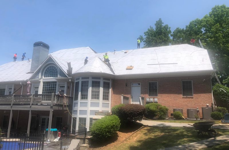 Large brick home with the roof covered in underlayment during a replacement