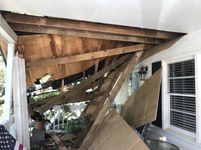Daylight visible through the torn-open porch roof rafters from underneath