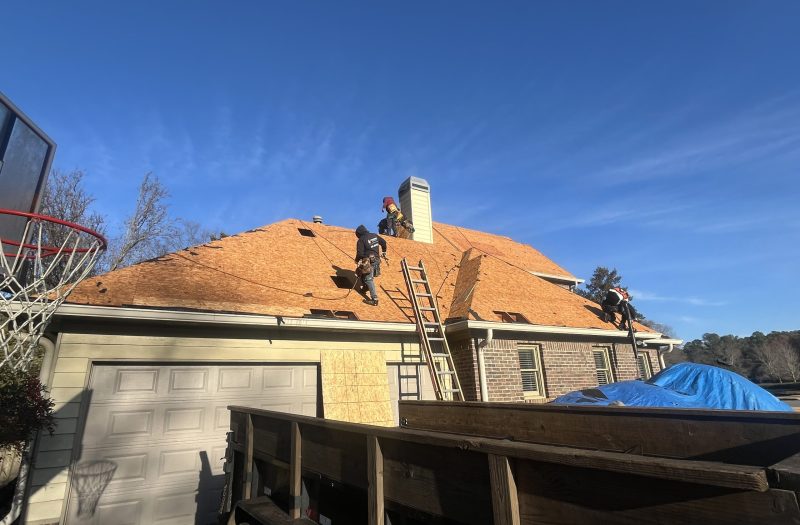 Brick two story home with the roof stripped to bare underlayment and a ladder against the eave
