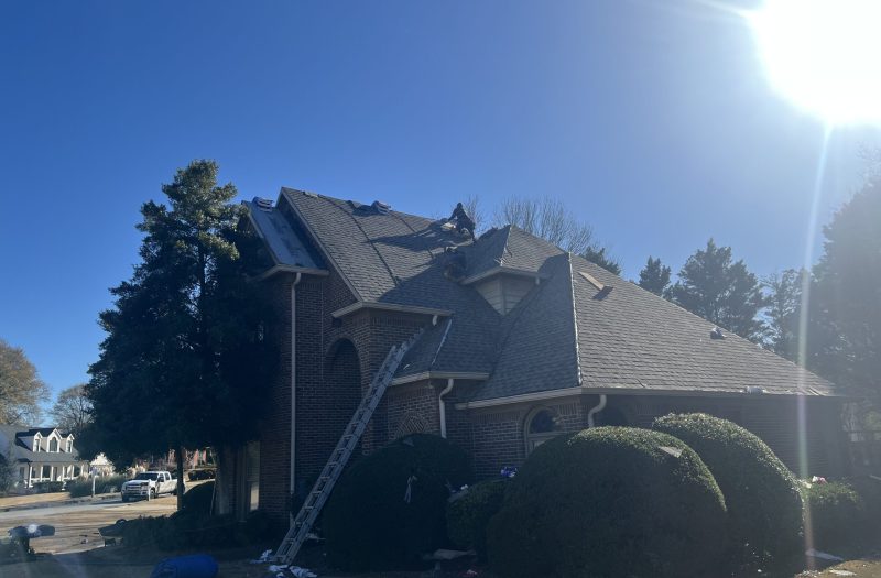 Side of a brick home with new dark shingles partly laid over the underlayment