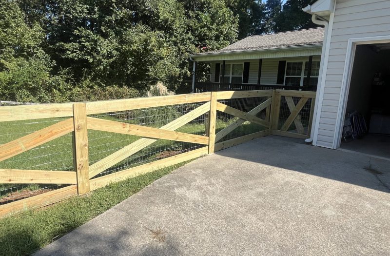 Split rail fence lining a concrete driveway up to a house