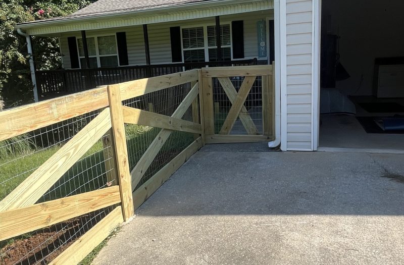 Split rail fence and gate at the end of a driveway beside a garage