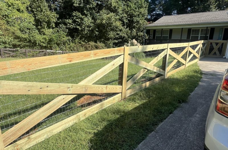 Wood split rail fence with wire mesh running along a lawn beside a driveway